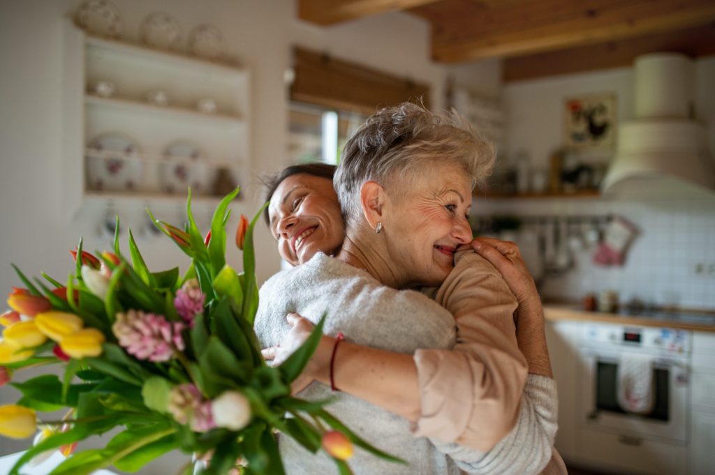 Happy senior mother hugging adult daughter indoors at home, mothers day or birthday celebration