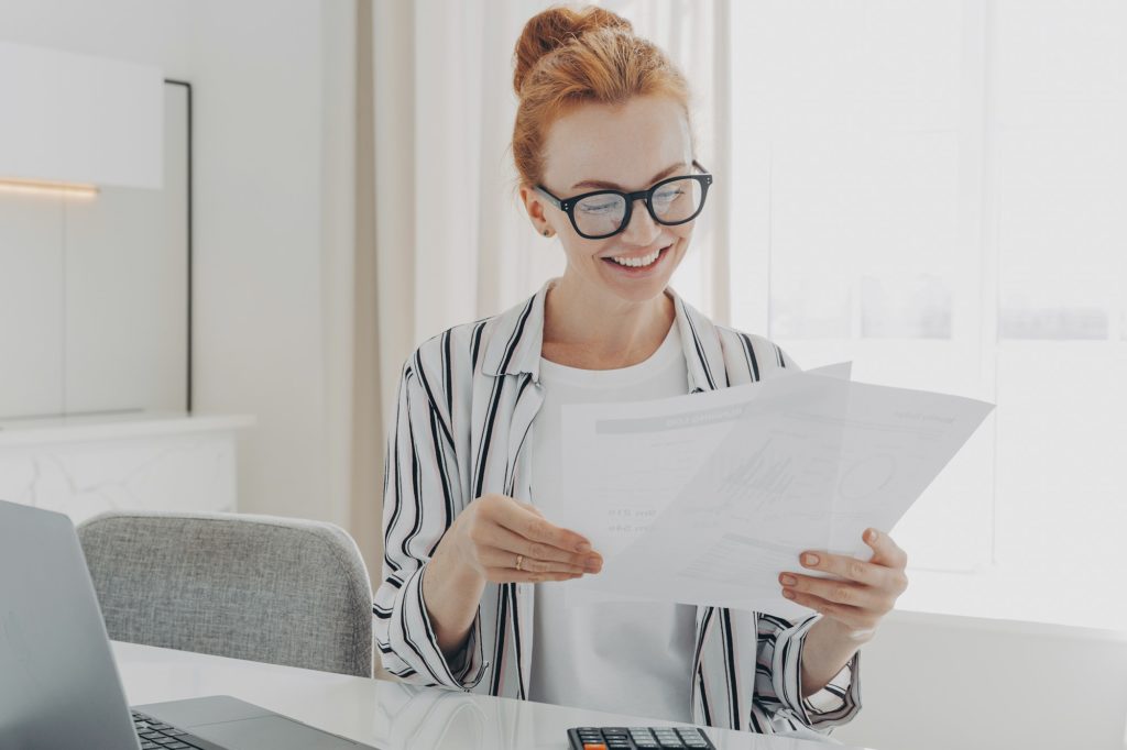 Happy smiling caucasian woman reading good news in financial documents while managing family budget