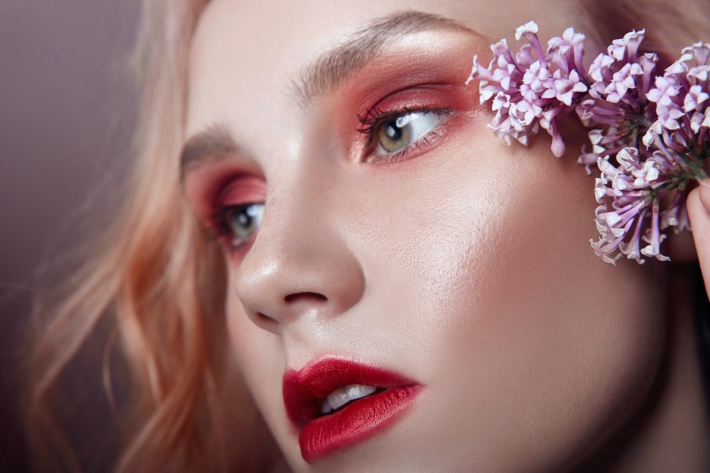 Portrait of a blonde woman with flower petals on her face closeup, bright red makeup